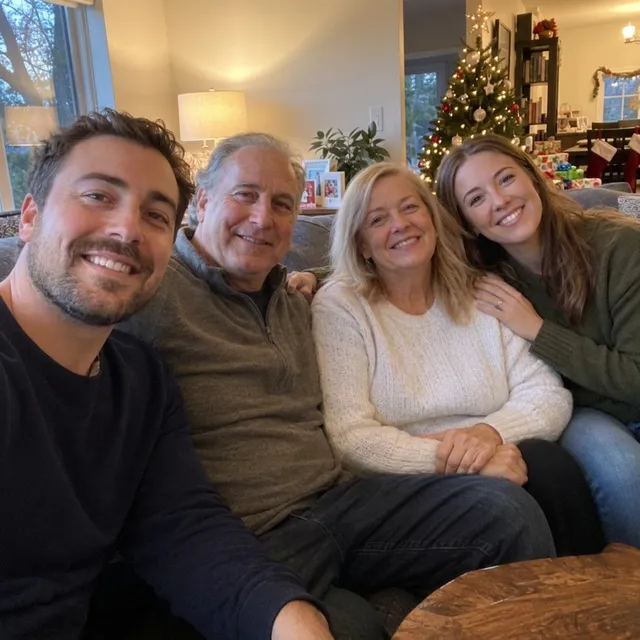 The same four people with a small Christmas tree partly hidden behind one head