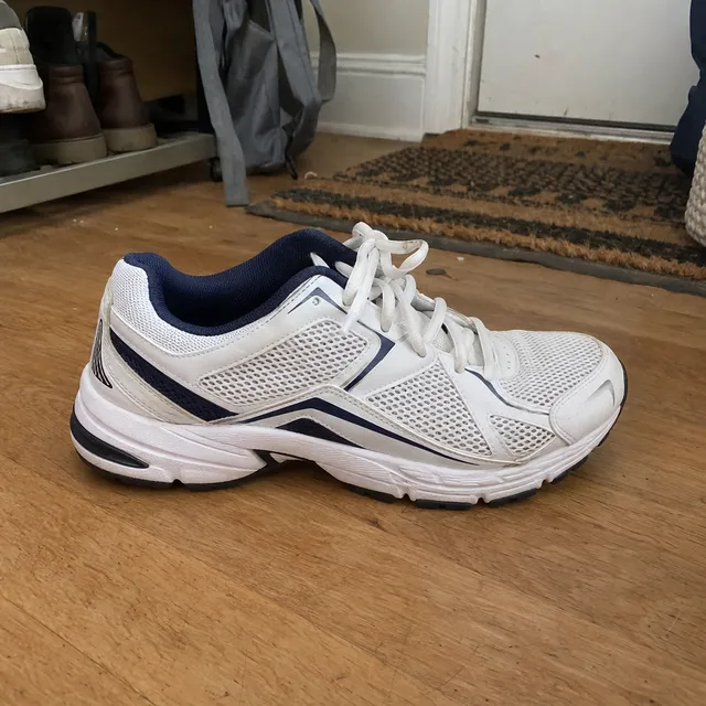 Synthetic smartphone photo of a white and navy running sneaker on a wooden floor next to a doormat