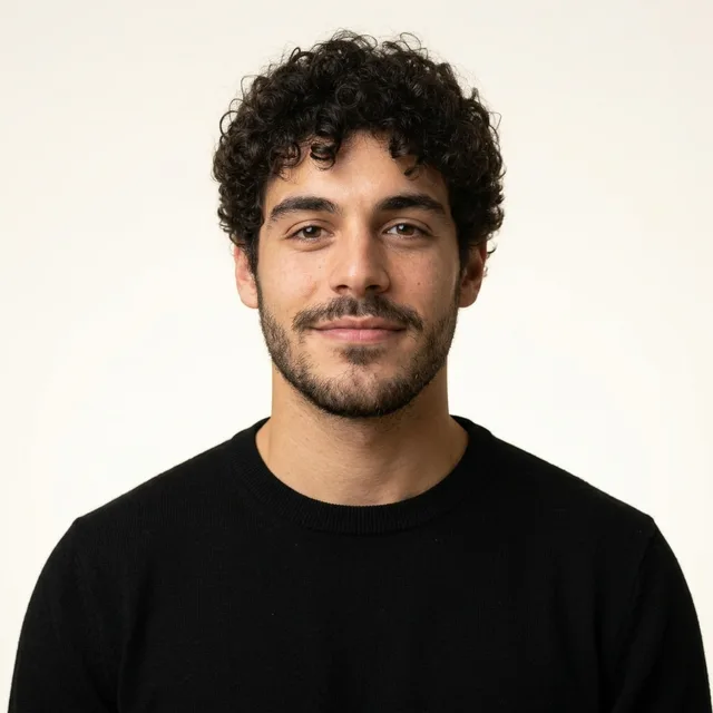 The young man in a black crew-neck sweater on the same warm white backdrop