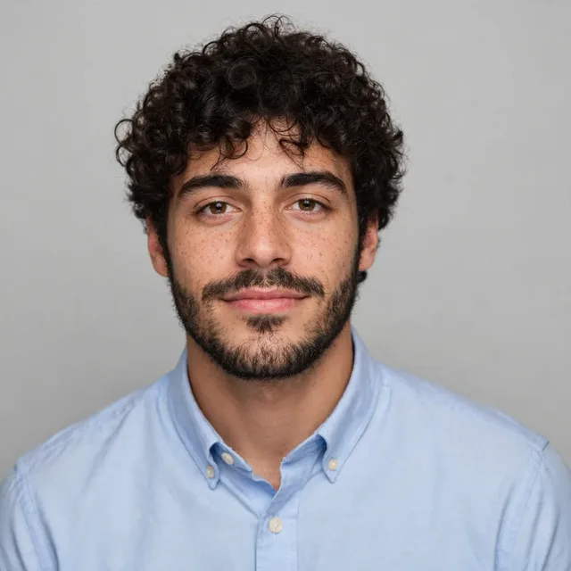 The same young man in a light blue shirt on light grey, with a fuller beard