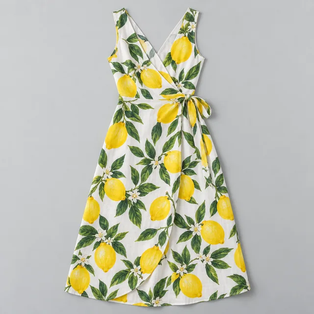 Synthetic product photo: a sleeveless white wrap dress with a print of large yellow lemons and green leaves