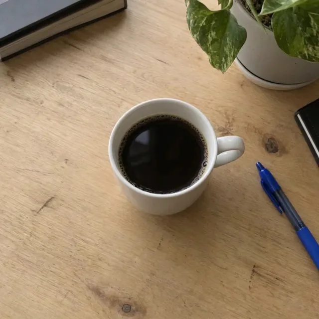 Dieselbe Tasse auf einem aufgeräumten Holzschreibtisch, nur mit Stift und Pflanze