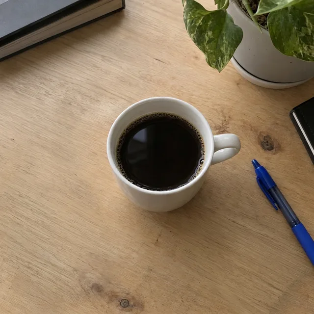 The same mug on a clean wooden desk with only the pen and plant left