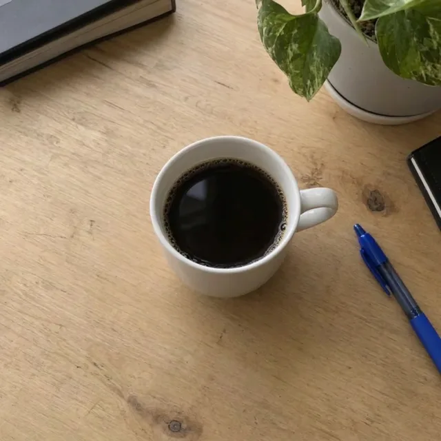 La même tasse sur un bureau en bois propre, avec seulement le stylo et la plante
