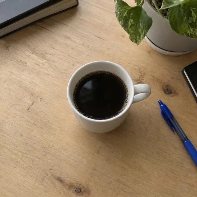 La stessa tazza su una scrivania di legno pulita, con solo la penna e la pianta