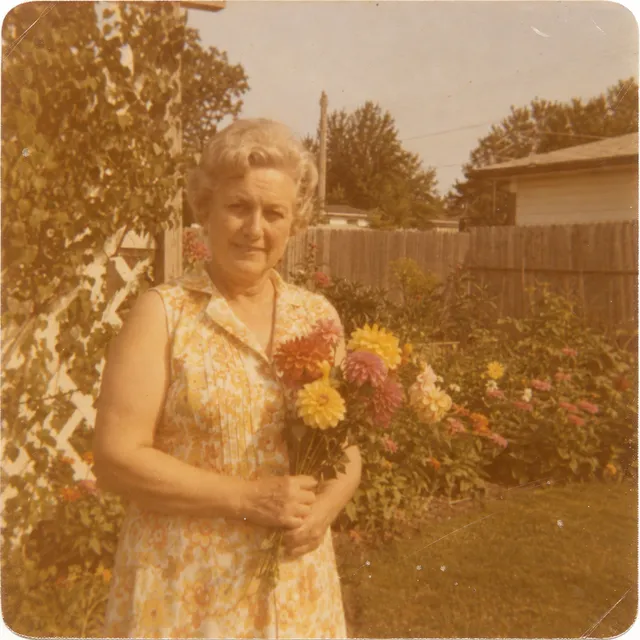 Synthetic scan of a faded 1970s colour snapshot: an older woman holding garden flowers, with a strong yellow-orange colour cast, scratches and rounded corners