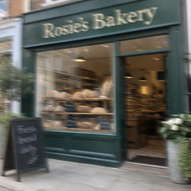 Shaky photo of a green bakery front with a sign and a sidewalk chalkboard
